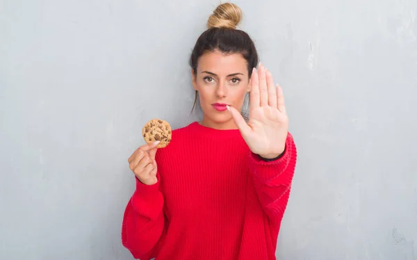 防衛ジェスチャー 深刻な自信を持って式に一時停止の標識をやって開いた手のチョコレート チップ クッキーを食べて灰色グランジ壁を越えて若い成人女性 — ストック写真