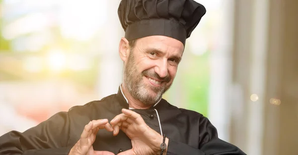 Senior cook man, wearing chef hat happy showing love with hands in heart shape expressing healthy and marriage symbol