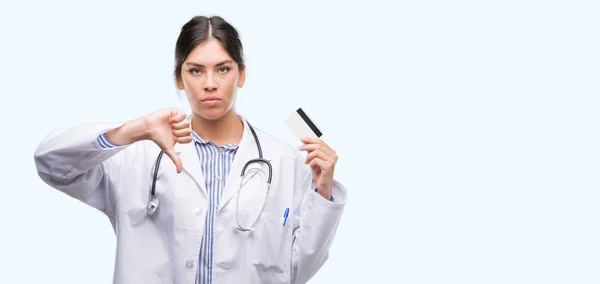 年轻的西班牙裔医生妇女持有信用卡与愤怒的脸 否定的符号显示不喜欢拇指向下 拒绝概念 — 图库照片