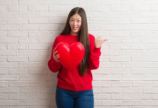 Молодая Китаянка Влюбленная Кирпичную Стену Держит Красное Сердце Указывая Пальцем — стоковое фото