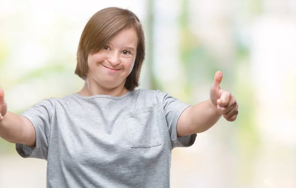 Young adult woman with down syndrome over isolated background approving doing positive gesture with hand, thumbs up smiling and happy for success. Looking at the camera, winner gesture.