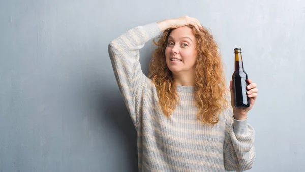 Joven Pelirroja Sobre Pared Grunge Gris Sosteniendo Botella Cerveza Estresada — Foto de Stock