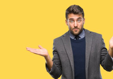 Genç yakışıklı iş adamı izole arka plan clueless ve şaşkın bir ifadeyle kollar ve eller ortaya çıkar üzerinden. Şüphe kavramı.