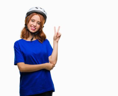 Mutlu yüz zafer işareti yaparken kameraya göz kırpıyor ile gülümseyen izole arka plan üzerinde bisikletçi kask giyen genç güzel kadın. İki numaralı.