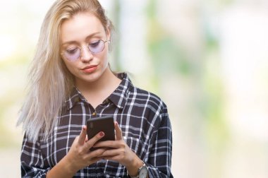 Sarışın genç kadın manifatura acımak yüz ciddi düşünüyorum üstünde kendine güvenen bir ifade ile izole arka plan üzerinde Smartphone kullanarak ileti gönderme