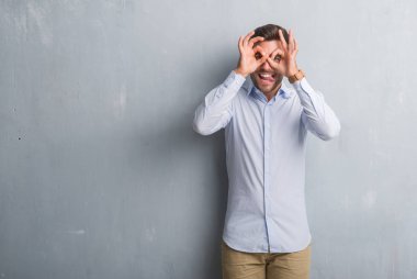 Yakışıklı genç iş adamı gri grunge üzerinde duvar giyen şık gömlek, dilini parmaklarının arasından baktığını yapışmasını dürbün gibi ok jest yapıyor. Deli ifade.