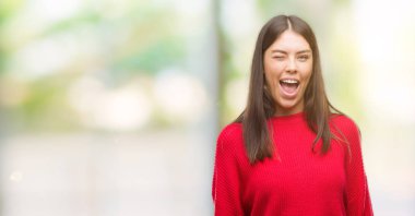 Kırmızı kazaklı seksi bir ifadeyle, neşeli ve mutlu yüzünü kameraya bakarak göz kırpıyor giyen genç güzel İspanyol.