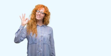 El ve parmak ile ok işareti yapıyor olumlu gülümseyen genç redhead bussines kadın. Başarılı ifade.