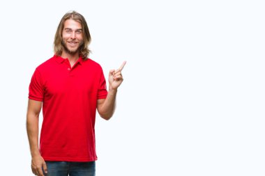 Kameraya bakarak yan el ve parmak ile işaret eden genç yakışıklı adam yüzünde kocaman bir gülümseme ile izole arka plan üzerinde uzun saçlı.