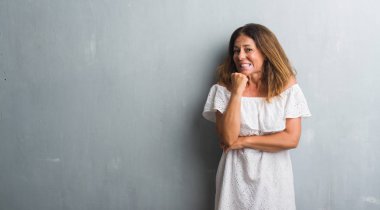 Stresli ve gergin elle çivi ısırma ağzına seyir gri grunge duvarın üzerinden duran orta yaş İspanyol kadın. Anksiyete sorunu.