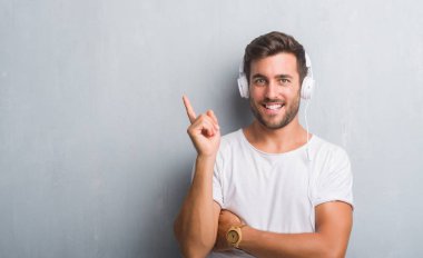 El ve parmak ile tarafına işaret çok mutlu müzik dinlerken kulaklık giyen gri grunge duvarın üzerinden yakışıklı genç