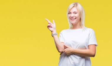 Kameraya bakarak yan el ve parmak ile işaret yüzünde kocaman bir gülümseme ile izole arka plan üzerinde beyaz t-shirt giyen genç güzel sarışın kadın.