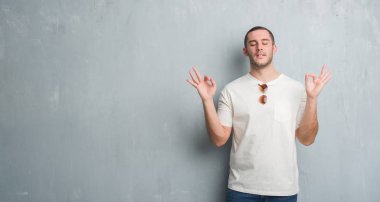 Güneş gözlüğü takıyor gri grunge duvarın üzerinden beyaz delikanlı rahatla ve gülümseyen gözlerle kapalı parmak jestle meditasyon yapıyor. Yoga kavramı.