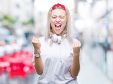 İzole arka plan kutlama üzerinden müzik kulaklık giyen genç sarışın kadın şaşırttı ve başarı için kaldırdı kollarını açarak hayret ve gözleri açık. Kazanan kavramı.