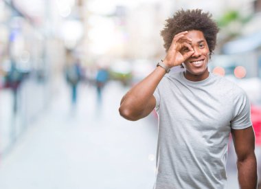 Afro Amerikalı adam gülümsüyor, parmakları ile mutlu yüz üzerinden seyir göz el ile ok jest yapıyor izole arka plan üzerinde.