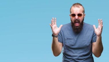 Üzerinde güneş gözlüğü takmış Genç beyaz hipster adam arka plan deli izole ve deli bağırarak ve agresif ifade ve silah kaldırdı bağırıyor. Hayal kırıklığı kavramı.