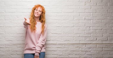 Tebrik ve konuksever dost sunan karşılıklı gülümseyen tuğla duvarın üzerinden duran genç Kızıl saçlı kadın. Başarılı iş.