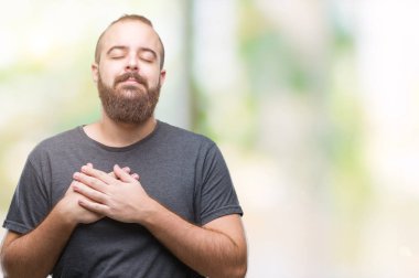 Göğüs kapalı gözler ve yüzünde minnettar jest ile izole arka plan ile gülümseyen üzerinde genç beyaz hipster adam eller. Sağlık kavramı.