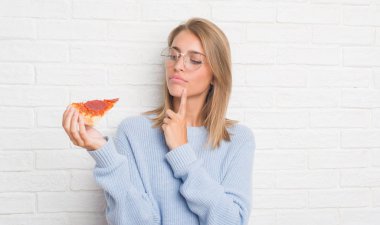 Güzel ve genç birbayan pizza dilimi ciddi bir yüz düşünme hakkında soru, çok karışık fikir yemek beyaz tuğla duvarın üzerinden