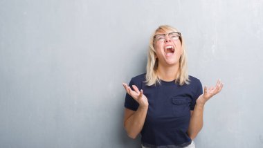 Yetişkin beyaz kadın çılgın ve kızgın bağırarak ve agresif ifade ve silah kaldırdı bağırmaya gözlüklü grunge gri duvar yüzünden. Hayal kırıklığı kavramı.