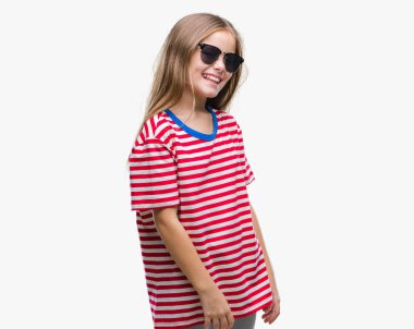 Genç güzel kız uzak tarafına yüzünde, doğal ifade gülümseme ile seyir izole arka plan üzerinde güneş gözlüğü takıyor. Kendine güvenen gülüyor.