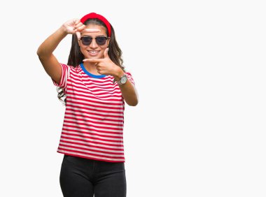 Genç güzel Arap kadın elle yapma çerçeve ve parmakları ile mutlu yüz gülümseyen izole arka plan üzerinde güneş gözlüğü takıyor. Yaratıcılık ve Fotoğrafçılık kavramı.