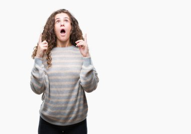 İzole arka plan üzerinde kış kazak giyen genç kız hayran ve yukarıya bakıp parmakları ile işaret şaşırttı ve silah kaldırdı güzel esmer kıvırcık saç.