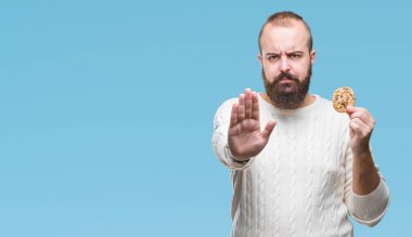 Genç hipster man açık eliyle dur işareti ile ciddi ve kendine güvenen ifade, savunma jest yapıyor izole arka plan üzerinde çikolata çerez yemek