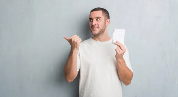 Young Caucasian Man Grey Grunge Wall Showing Notebook Pointing Showing — Stock Photo, Image