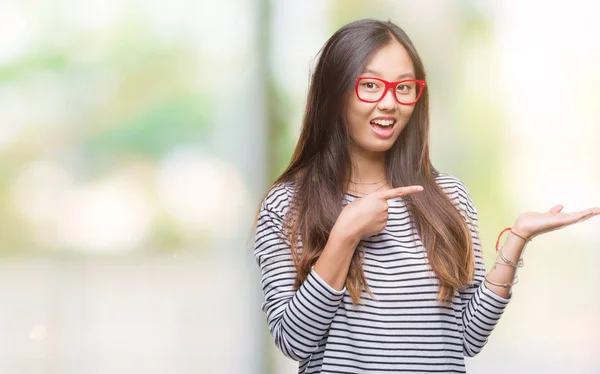 年轻的亚洲妇女戴着眼镜在孤立的背景下惊讶和微笑的相机 而用手和手指指着 — 图库照片