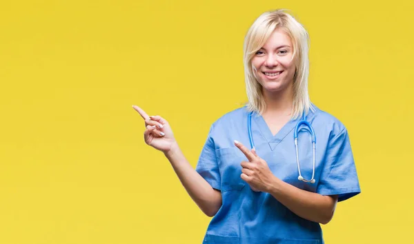 年轻美丽的金发医生妇女穿着医疗制服在孤立的背景微笑着 看着相机指着两个手和手指的侧面 — 图库照片