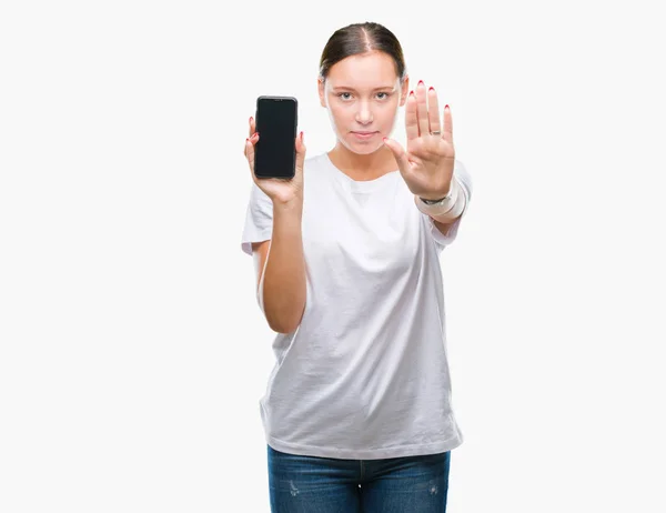 年轻美丽的高加索妇女显示智能手机屏幕在孤立的背景与开放的手做停止标志与严肃和自信的表达 防御手势 — 图库照片