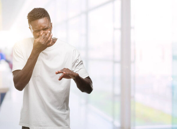 Молодой африканский американец в белой футболке, пахнущий чем-то вонючим и отвратительным, невыносимым запахом, затаив дыхание пальцами на носу. Концепция дурных запахов
.