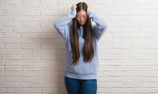 Genç Chinise kadın beyaz tuğla duvar çünkü umutsuz ve stresli baş ağrısı acı acı ve migren. Ellerini kafasına.