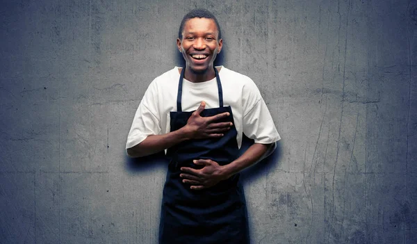 African man shop owner wearing apron confident and happy with a big natural smile laughing