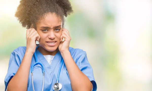 Young afro american doctor woman over isolated background covering ears with fingers with annoyed expression for the noise of loud music. Deaf concept.