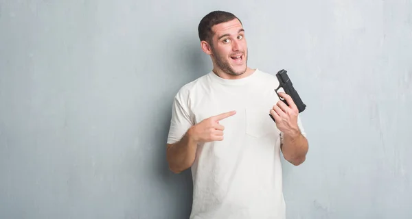 Joven Caucásico Criminal Hombre Sobre Gris Grunge Pared Sosteniendo Arma —  Fotos de Stock