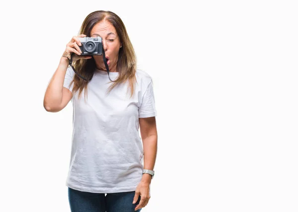 Middle age hispanic woman taking pictures using vintage photo camera over isolated background scared in shock with a surprise face, afraid and excited with fear expression