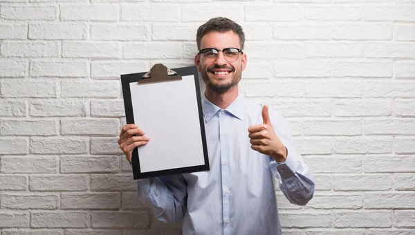 Joven Hombre Negocios Adulto Sobre Pared Ladrillo Sujetando Portapapeles Feliz —  Fotos de Stock