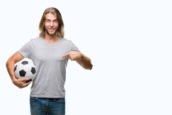 Young handsome man with long hair over isolated background holding football ball with surprise face pointing finger to himself