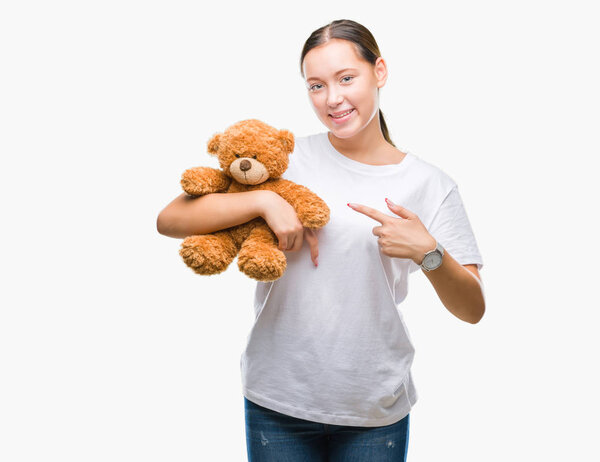 Young caucasian woman holding teddy bear over isolated background very happy pointing with hand and finger