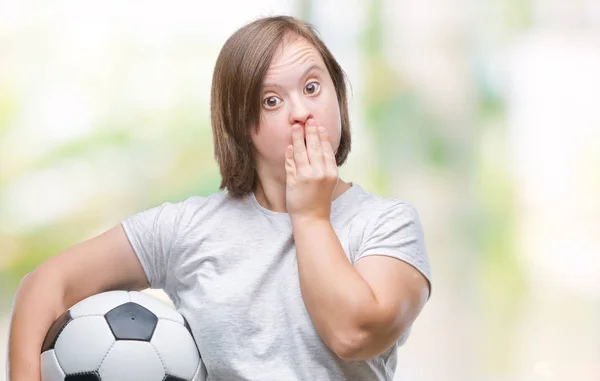 Young adult woman with down syndrome holding soccer football ball over isolated background cover mouth with hand shocked with shame for mistake, expression of fear, scared in silence, secret concept
