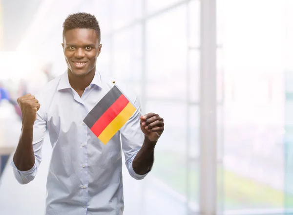 感情を応援して誇りに思って叫んで 勝利と非常に興奮して 成功を祝うドイツの旗を保持している若いアフリカ系アメリカ人 — ストック写真