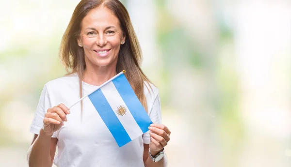 孤立した背景に立っていると自信を持って歯を見せて笑顔で笑っている幸せそうな顔でアルゼンチンの旗を保持している中年ヒスパニック系女性 — ストック写真