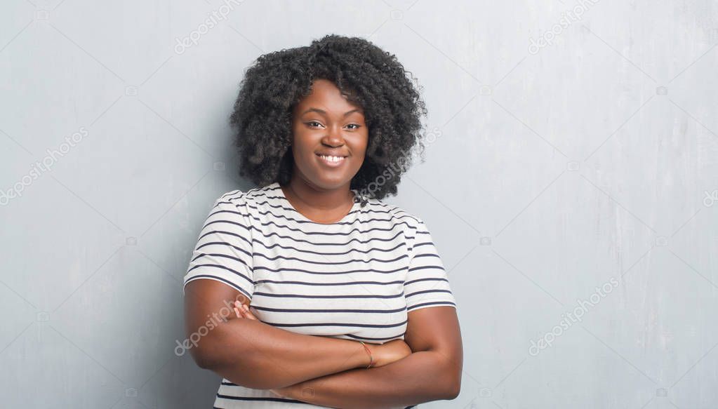 Young african american plus size woman over grey grunge wall happy face smiling with crossed arms looking at the camera. Positive person.