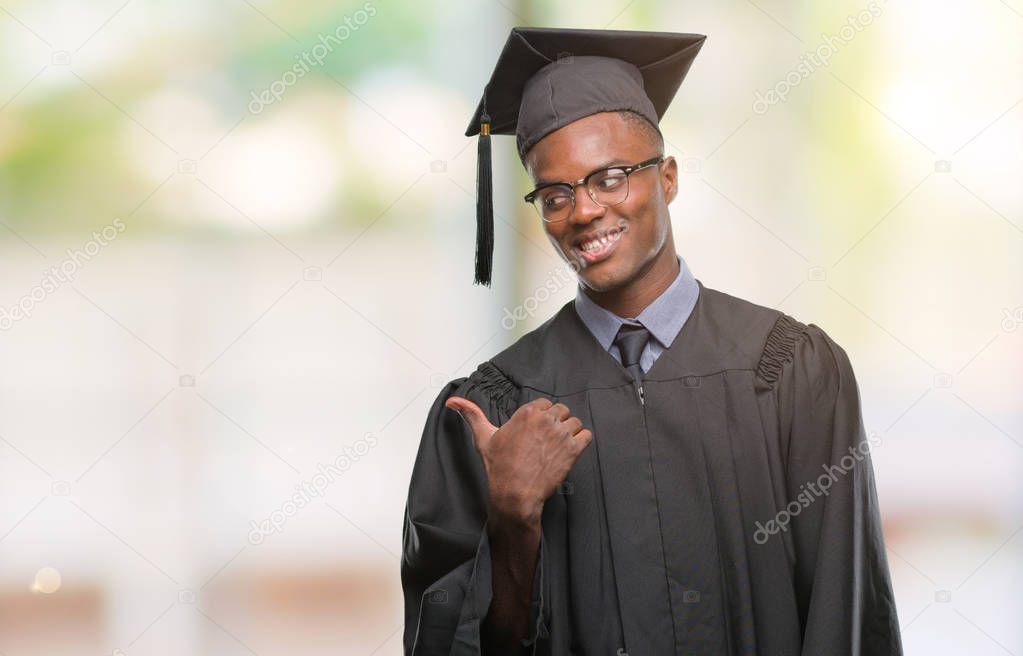 Young graduated african american man over isolated background smiling with happy face looking and pointing to the side with thumb up.