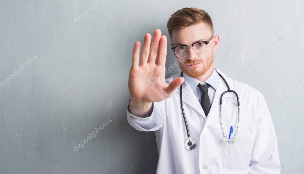 Young redhead doctor man over grey grunge wall with open hand doing stop sign with serious and confident expression, defense gesture
