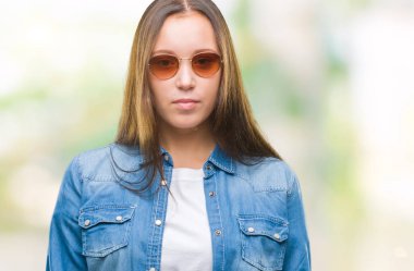 Yüzünde ciddi bir ifade ile izole arka plan üzerinde güneş gözlüğü takmış genç güzel beyaz bir kadın. Basit ve doğal kameraya bakıyor.