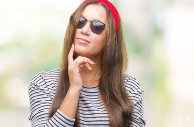 Çene düşünme hakkında soru, dalgın ifade üzerine el ile izole arka plan üzerinde güneş gözlüğü takmış genç güzel beyaz bir kadın. Düşünceli yüzüyle gülümsüyor. Şüphe kavramı.