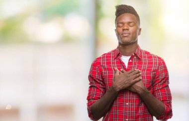 Göğüs kapalı gözler ve yüzünde minnettar jest ile genç Afro-Amerikan adam ile gülümseyen izole arka plan üzerinde eller. Sağlık kavramı.